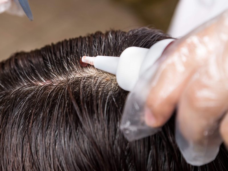 Closu-up of hair dresser applying chemical hair color dye onto hair roots in salon