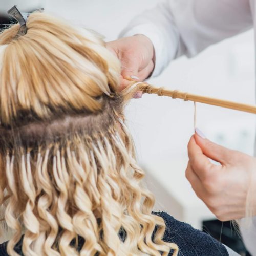 Hairdresser makes hairstyle close-up on blond hair of beautiful woman